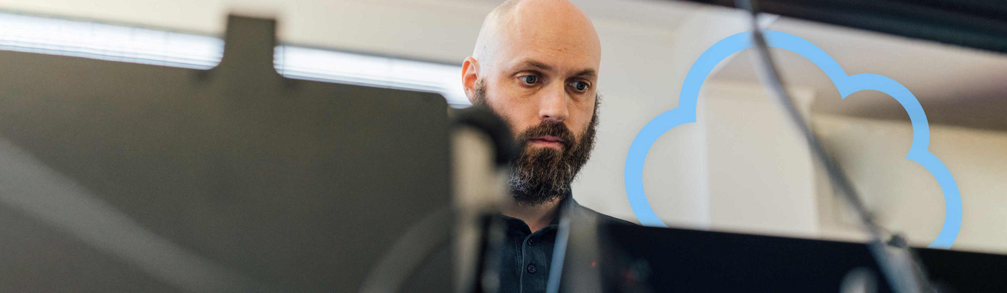 A Datacom technician with a beard working on a laptop with a floating cloud
