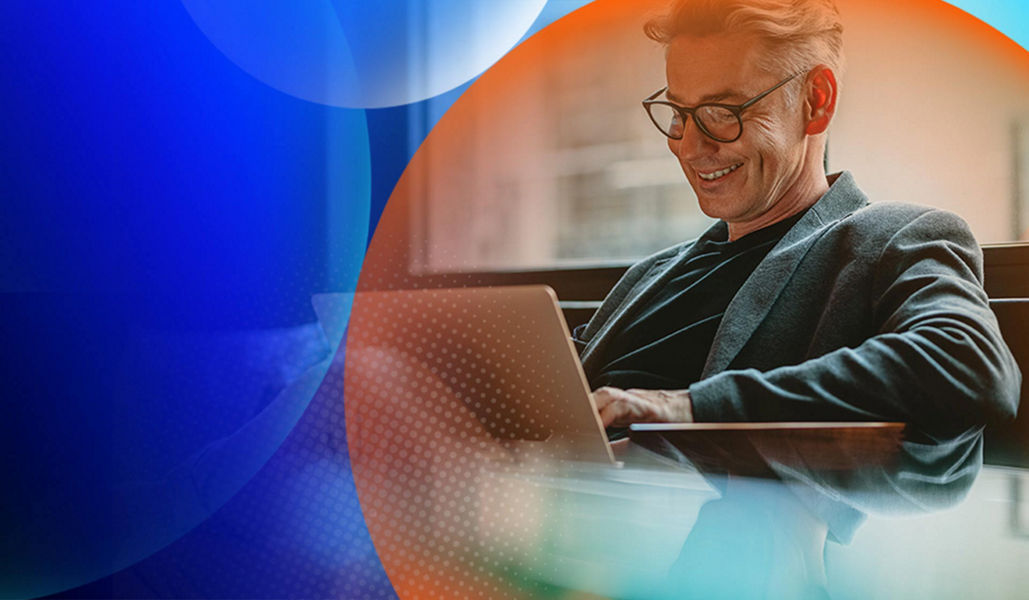 Man sitting on a couch typing on a laptop while smiling with an orange and blue lens overlay