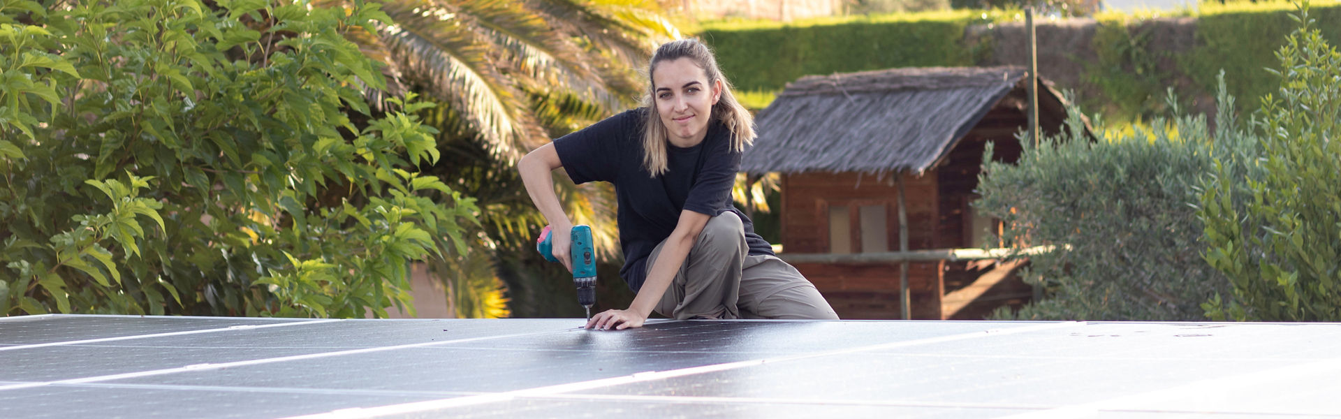 Woman installing solar panels on roof holding drill and smiling at camera on a nice sunny day