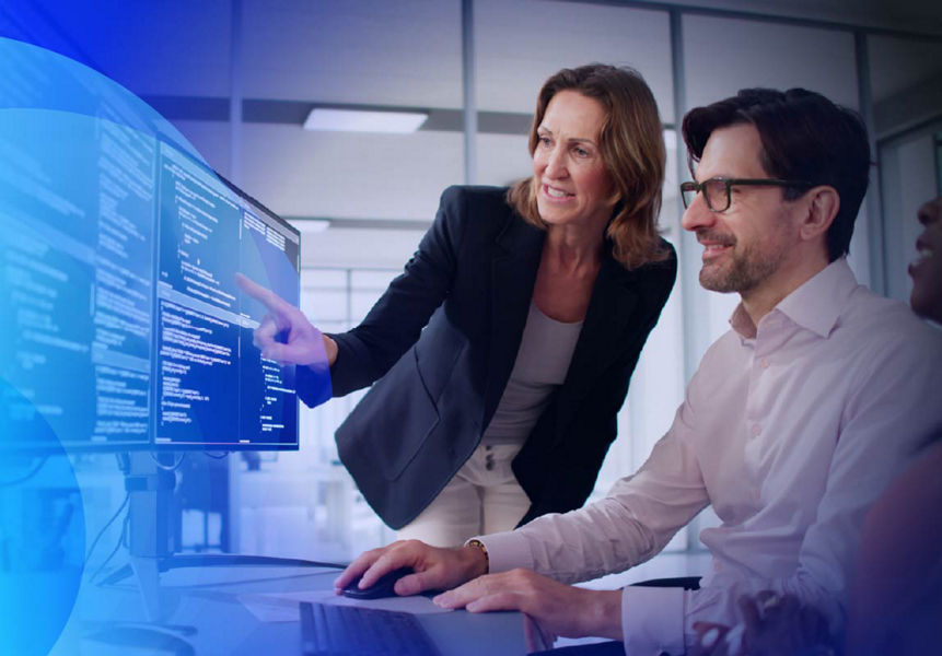 A team collaborating at a workstation, with a Programme Leader pointing on a dual-monitor setup.