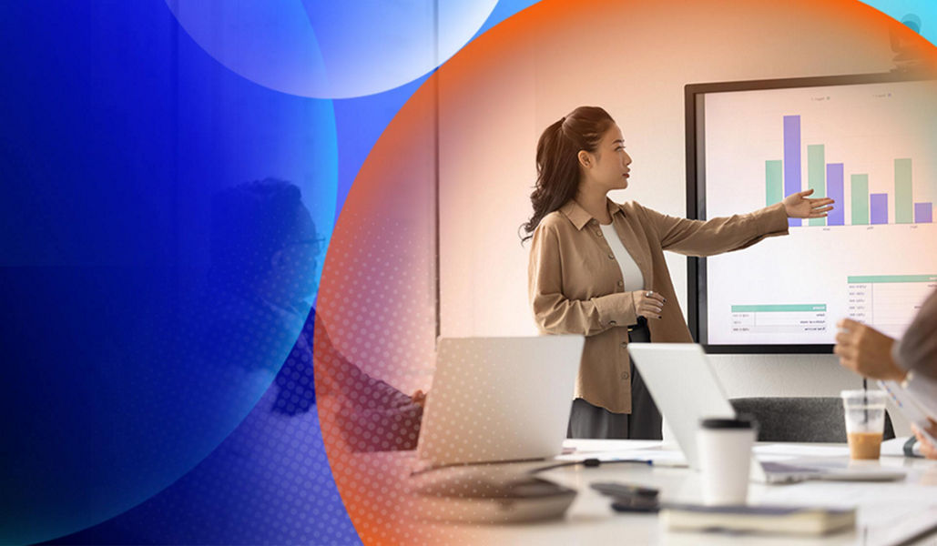 A woman in a meeting pointing at a big screen that has stats on it with and orange and blue lens overlay