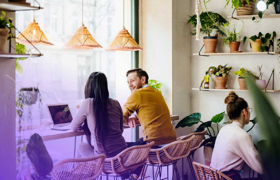Two people talking together in a cafe while on their latops