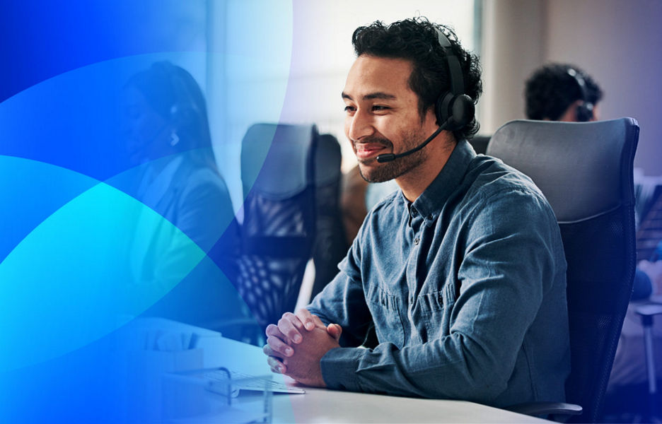 Man with headset sitting at office desk in front of a computer, listening to a customer.