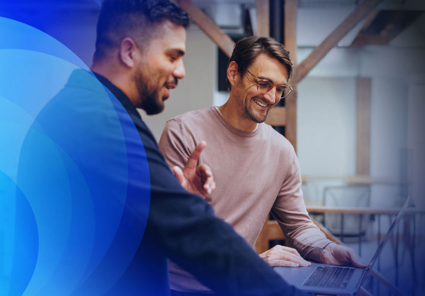 Two compliance professionals smiling while reviewing an application on a laptop.