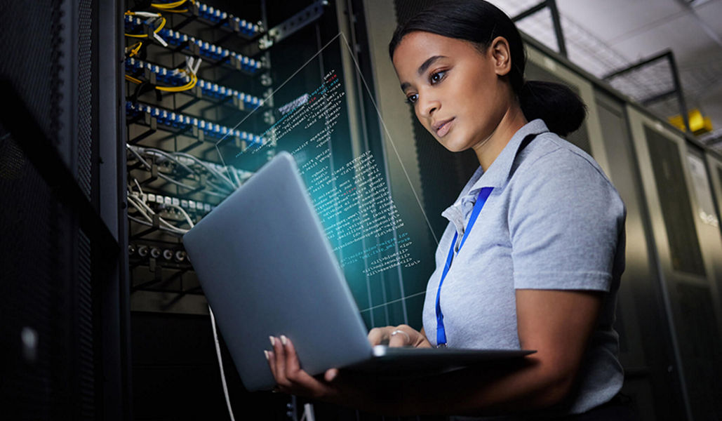 A woman holding a laptop in front of a electrics IT cabinet