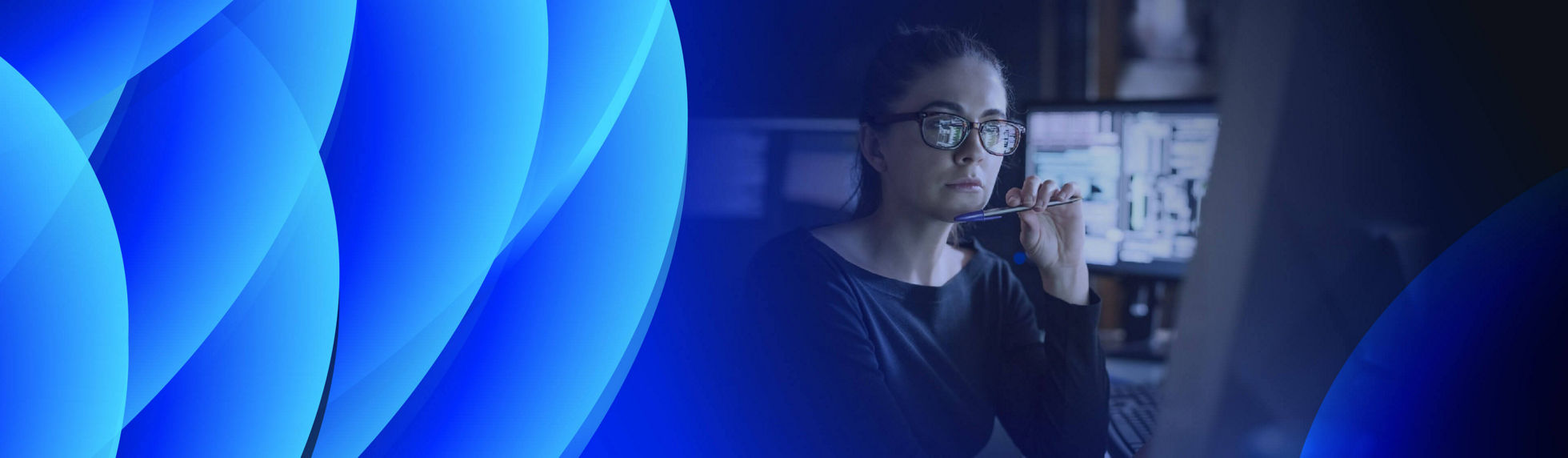 Woman looking at a monitor and surrounded with monitors in dark office