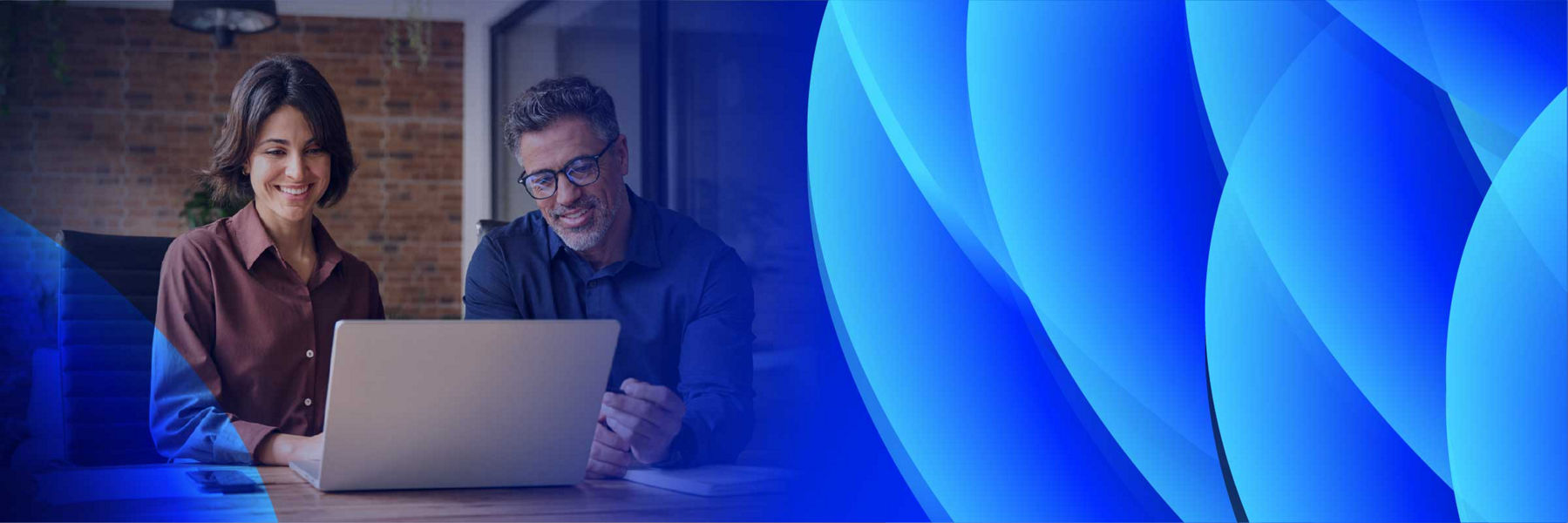 A man and a woman smiling as they work together on a laptop.