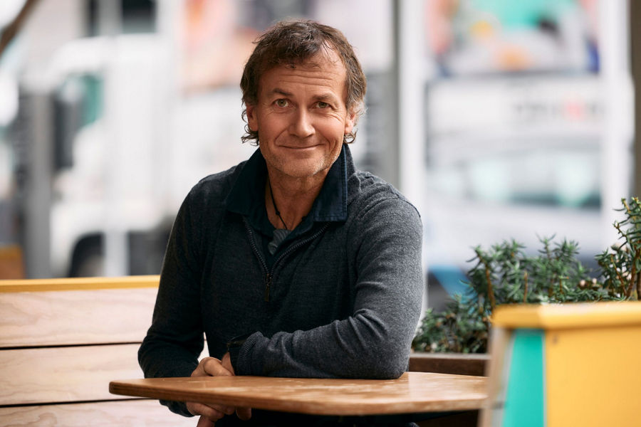 Profile photograph of Steve sitting on a bench resting his arm on a table