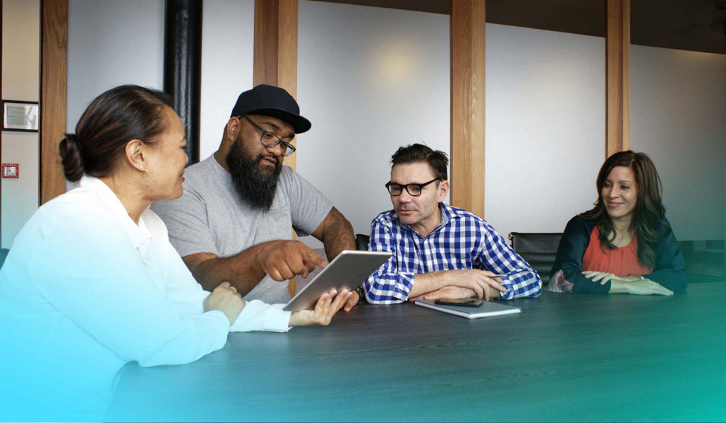 A team sitting around a table in a meeting room discussing and looking at a tablet