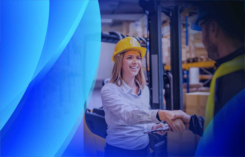 A smiling woman shaking hands with a supplier in a warehouse