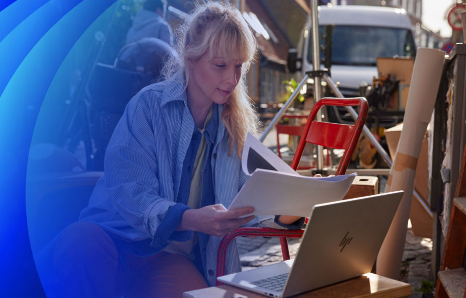 A professional women reviewing documents infront of a laptop on a busy outdoor film set