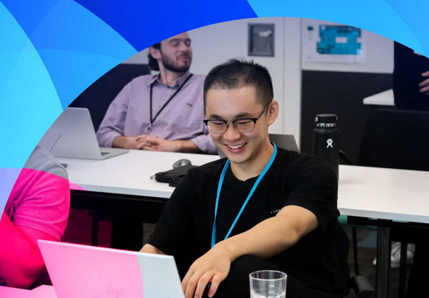 A smiling graduate pointing at a laptop