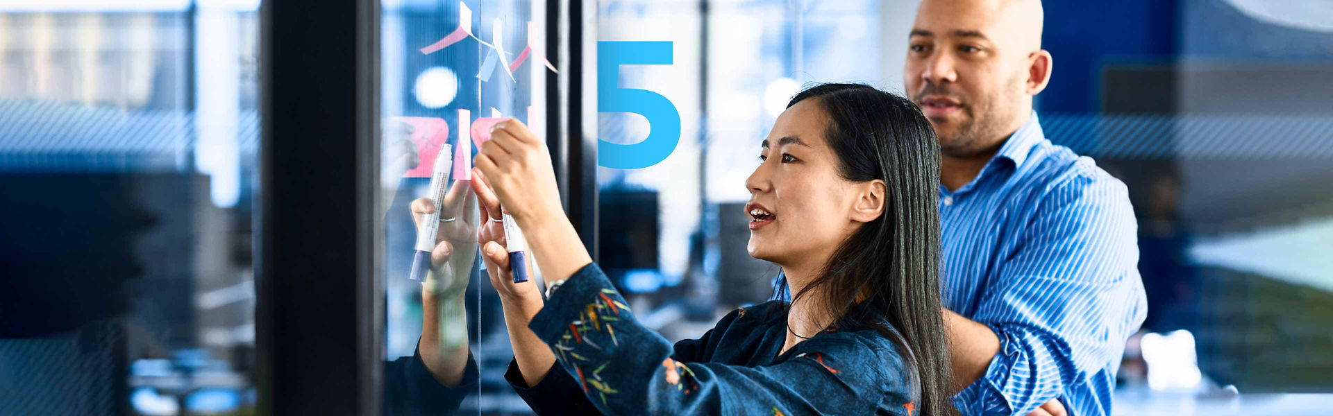 A woman sticking notes on glass with a colleague