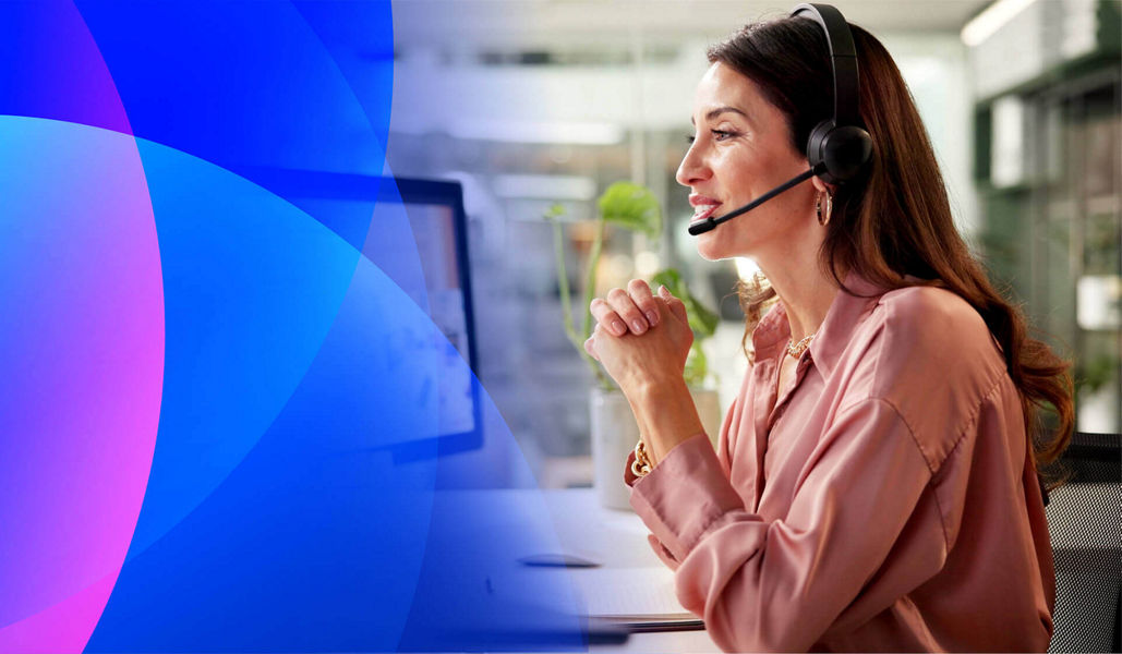 A woman sitting at a desl talking on a headset 