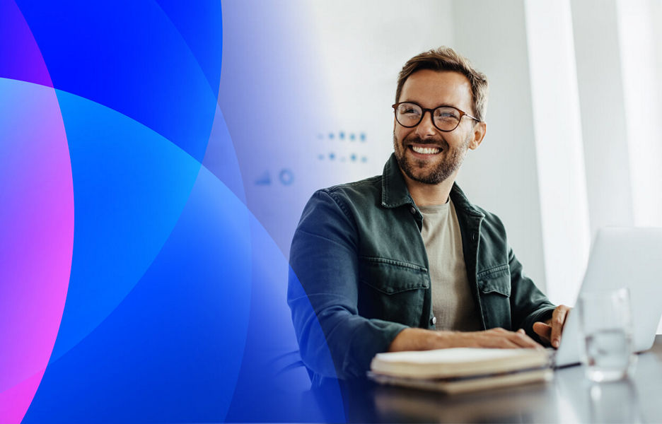 Smiling man in glasses working on a laptop in a bright office, with blue and pink abstract shapes on the left side of the banner.
