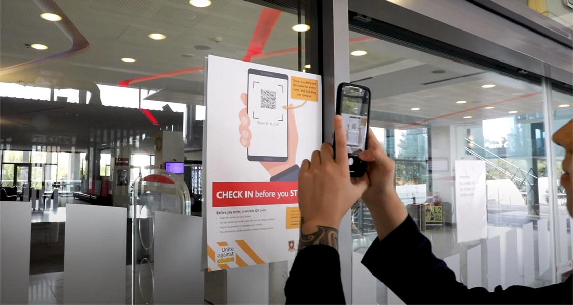 A person holds up their mobile phone to scan a QR code on a poster