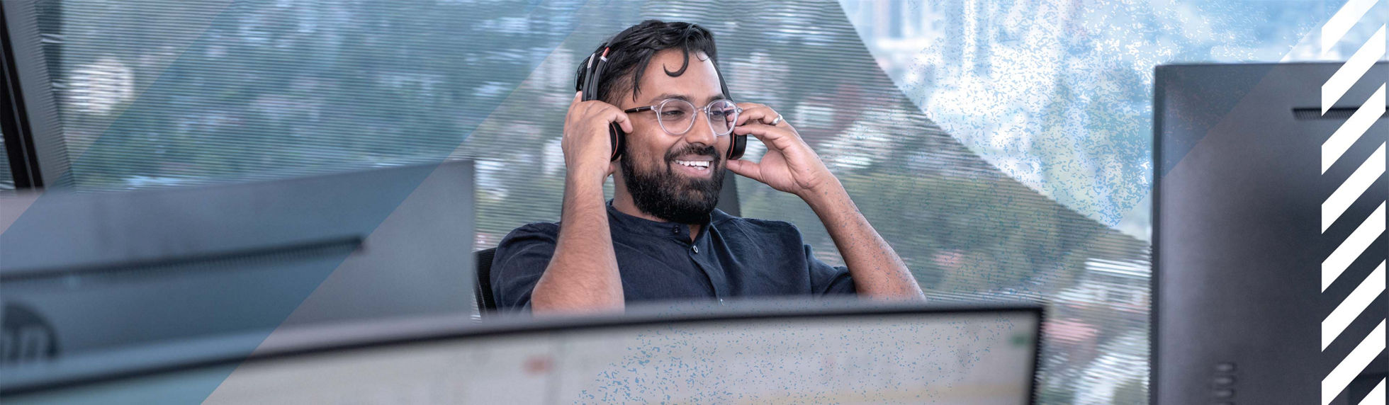 A man with a headset smiling while looking at a computer screen