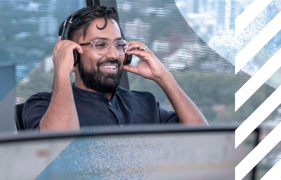 A man with a headset smiling while looking at a computer screen