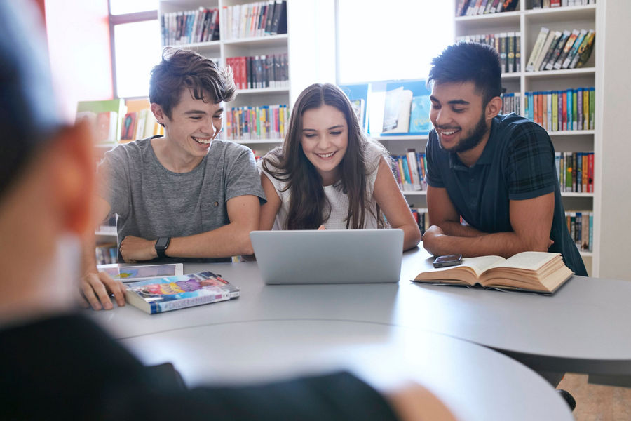 Three students sitting in library using a laptop
