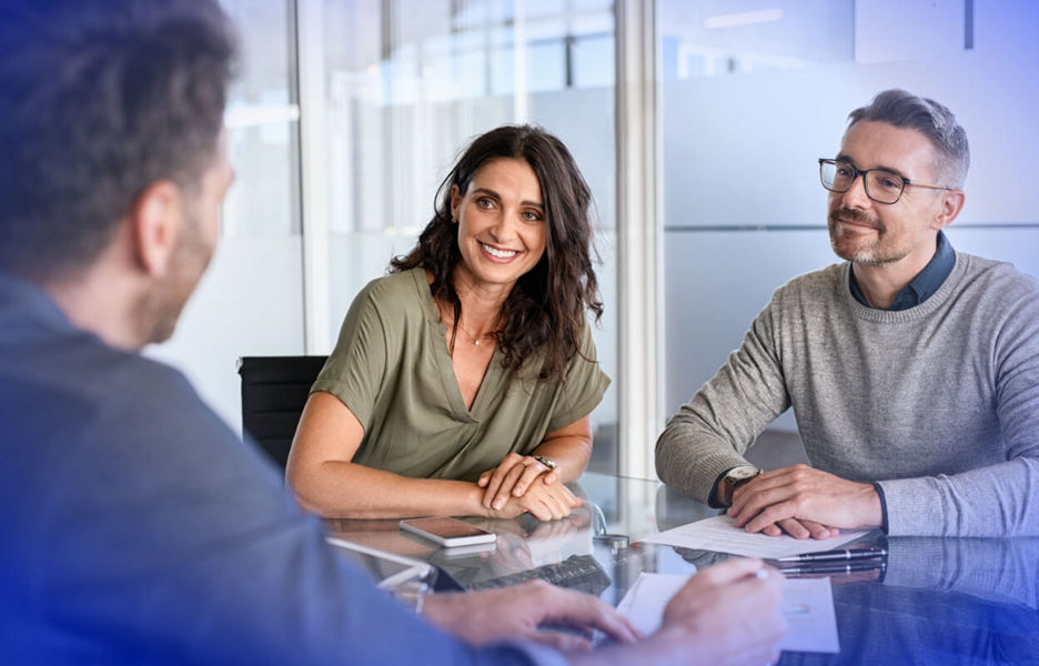 Three professionals seated around a table having a business meeting in a modern office setting. 