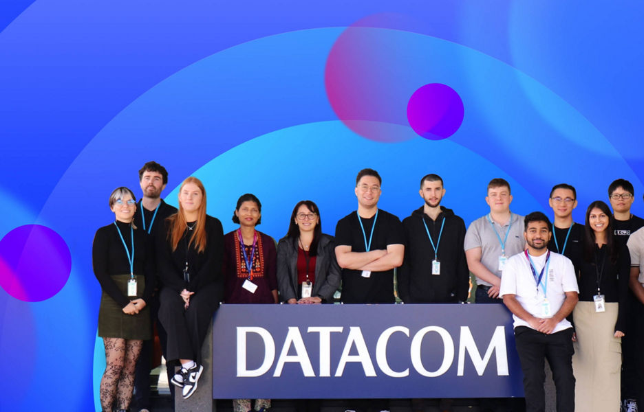 A group of smiling Datacom people in front of Datacom signage