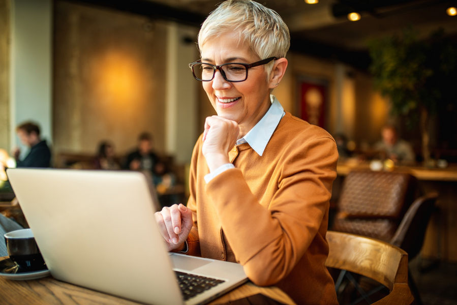 A lady with glasses smiling at a computer screen
