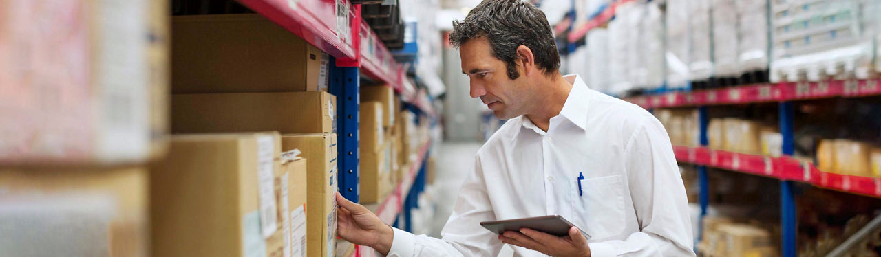 A man in a warehouse taking stock of boxes on a tablet