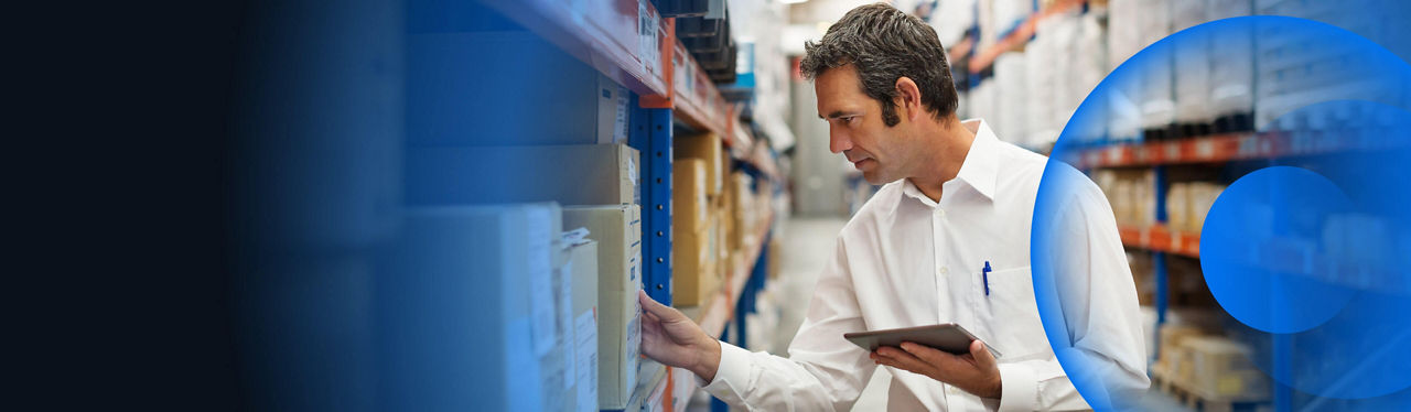 A man in a warehouse taking stock of boxes on a tablet
