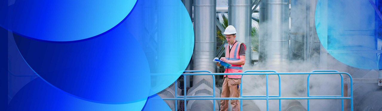 A worker standing on a walkway in front of large power station pipes