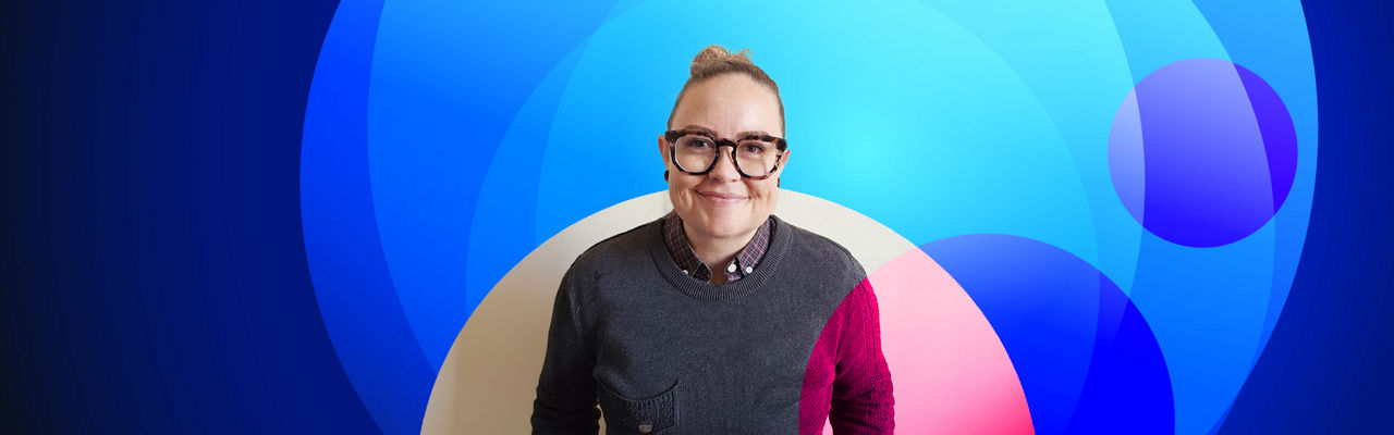 Nicola Lutze smiling standing against blank wall wearing a dark sweater, glasses, hair in a bun, with the discover spotlight banner design overlaid