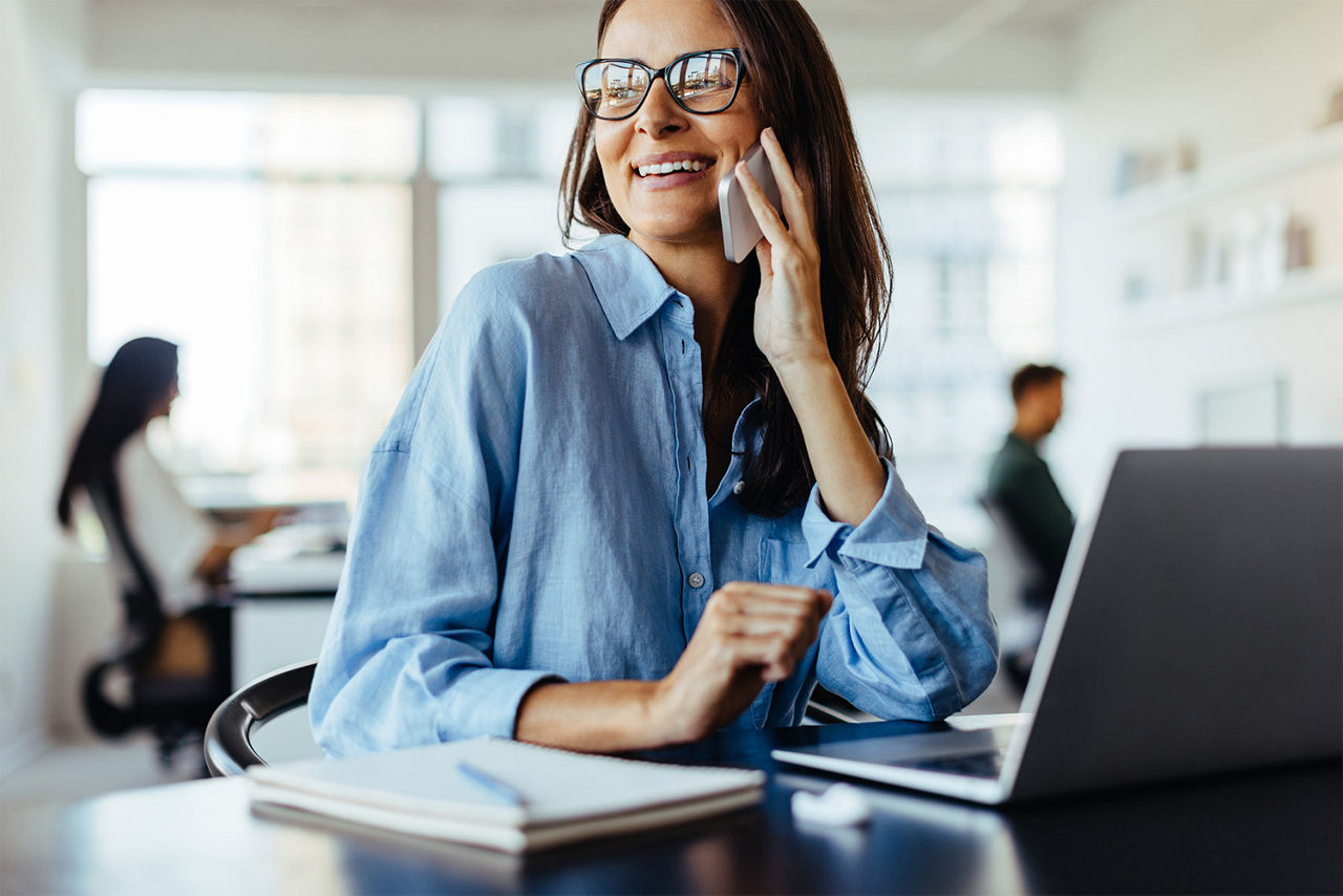 A woman talking on a phone sitting in front of a laptop.