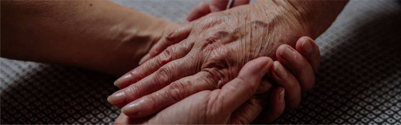 Hands of a senior woman and her daughter holding each other's hands together.