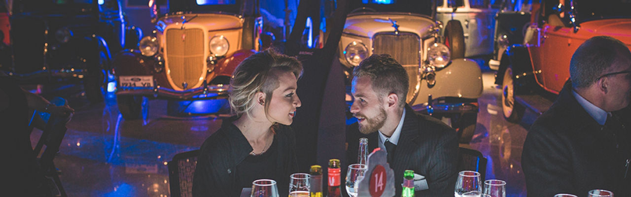 Two people talking to each other at a gala event with a backdrop of vintage cars