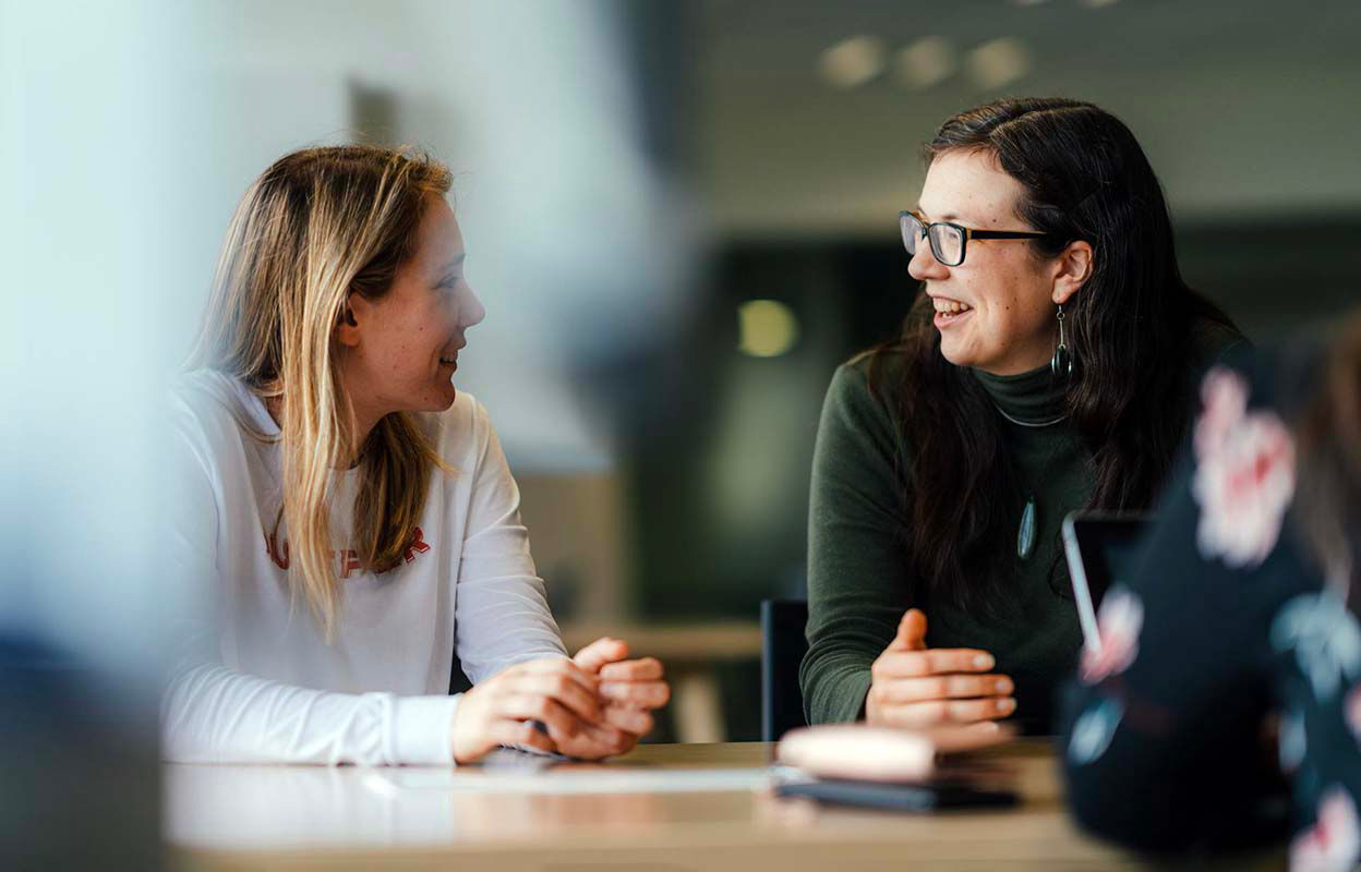 Two women sitting at a table, looking at eachother and discussing