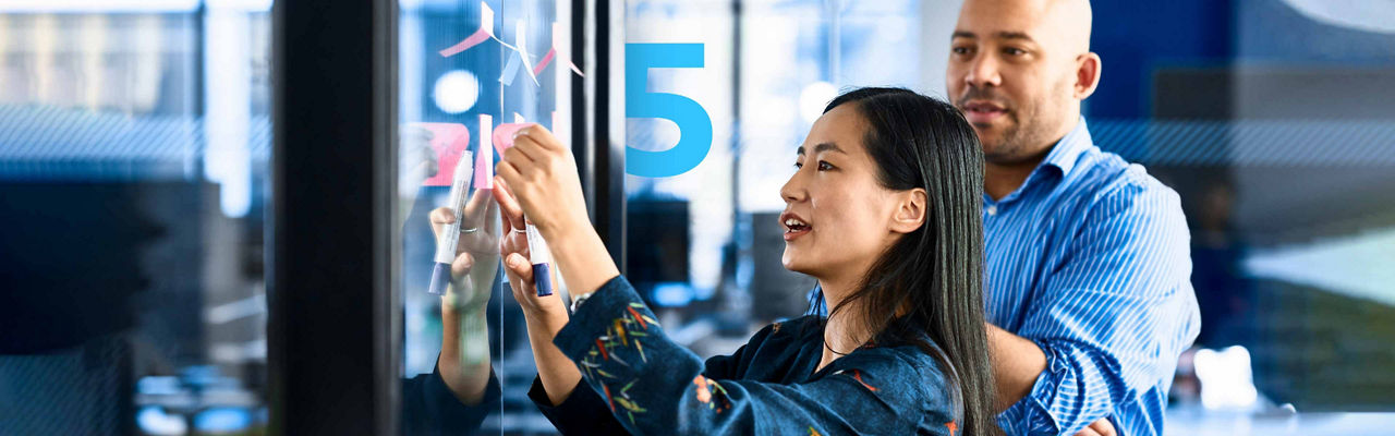 A woman sticking notes on glass with a colleague